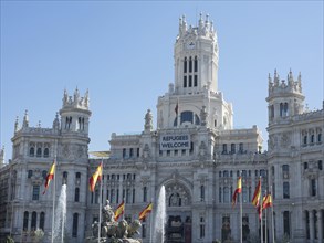 Monumental white palace with Spanish flags, spring fountain and a welcome banner for refugees,