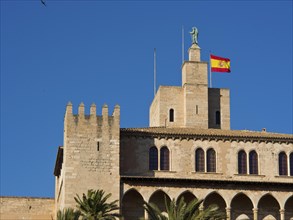 Historic building with stone tower and Spanish flag under a blue sky, palma de mallorca on the