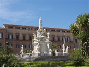 A magnificent fountain with statues in front of a historic building under a blue sky, palermo in