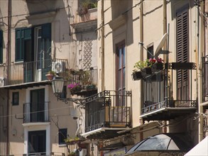 Historic buildings with balconies and shutters, decorated with flowers, in a Mediterranean setting,