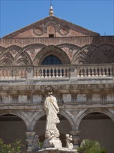 Historic facade with ornate arches and a large statue in the foreground, palermo in sicily with an