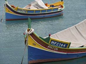 Close-up of two colourful boats in the clear water of a harbour in Malta, many colourful fishing