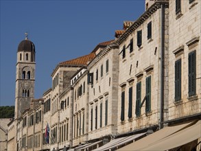 Row of historic buildings with a striking tower and green shutters, the old town of Dubrovnik with