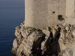 Robust coastal wall rising from the rocky shore and overlooking the sea, the old town of Dubrovnik