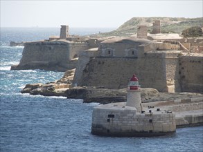 Coastline with historic lighthouse, parts of a fortress and the sea in the background, Valetta,