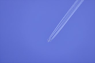 Passenger aeroplane, four-striped with condensation streaks in the blue sky, North
