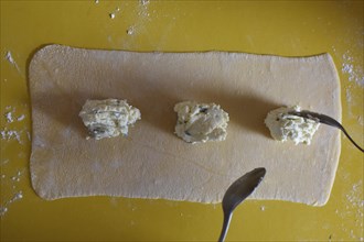 Preparation of fresh homemade pasta mezzaluna with ricotta and sage, filling is placed on the dough