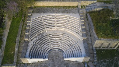Aerial view of an ancient amphitheatre with stone seating steps surrounded by green areas,