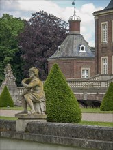 Stone sculpture in front of a historic castle with brick walls, green bushes and trees under a