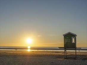 Sunset on the beach with a green wooden hut, peaceful sea and golden sky, evening mood on the beach