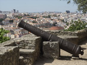 A rusty cannon leans against a stone wall overlooking an old town, Lisbon, Portugal, Europe