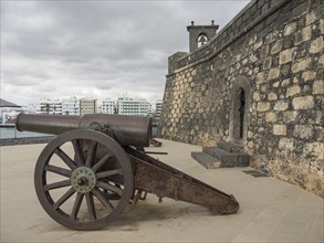 Old cannon in front of a historic stone wall under a cloudy sky, Lanzarote, Spain, Europe