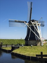 A black windmill stands on a sunny day on the banks of a canal in a green landscape, Enkhuizen,