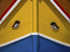 Close-up of a boat front, colourful with yellow and blue areas and eye motifs, colourful boats in a