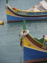 Two colourful traditional boats in the calm harbour waters of Malta, many colourful fishing boats