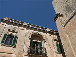 Facade of an old building with green shutters and decorative balcony, the town of mdina on the