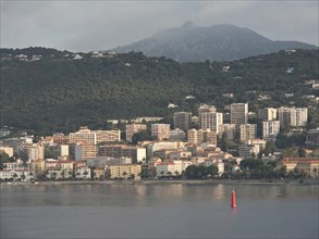 Coastal town with many residential buildings, mountains in the background and a calm sea, Corsica,