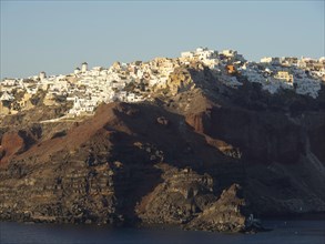 White houses on a rocky hill by the sea with a subtle evening mood in Greece, brown volcanic island