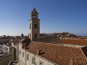 View of the city with a high church tower, historic buildings and red tiled roofs near the coast