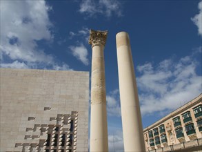 Two ancient columns in front of a building, surrounded by blue sky and clouds, Valetta, Malta,