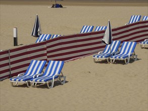 Beach where blue and white striped deckchairs, parasols and red partitions are arranged in rows,