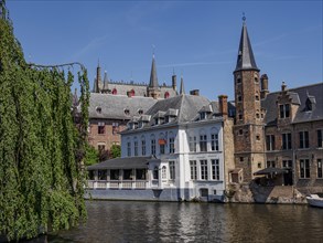 A building with a white facade and old brick towers by a river in sunny weather, historic houses