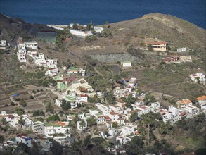 A small village on a hill with many white houses surrounded by green vegetation, with the sea
