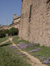 A fortress with old stone walls and a path lined with purple flowers, barcelona, spain