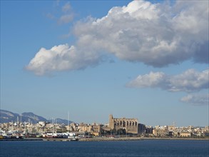 View of the city with church and buildings along the coast, under a blue sky with clouds, palma de