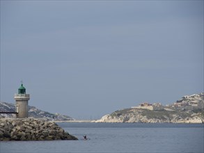 Lighthouse on a rocky coast in front of a calm sea and under a cloudy sky, Marseille on the