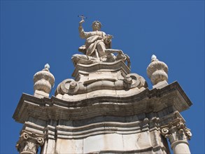 Detailed baroque statue with religious symbolism in front of a bright blue sky, palermo in sicily