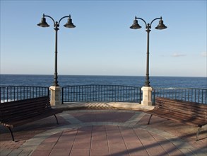 Two wooden benches and lanterns overlooking the calm sea under a clear sky, Valetta, Malta, Europe