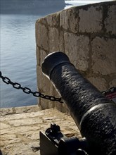 Close-up of a black cannon on an old stone wall overlooking the sea, the old town of Dubrovnik with