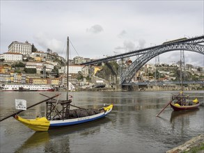 Boats on a wide river in front of a historic town and a big bridge on a cloudy day, Colourful