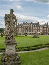 Stone sculpture in an elegant garden with a large castle in the background and cloudy sky, historic