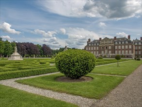 Symmetrical garden with manicured hedges and paths in front of a historic castle under a cloudy
