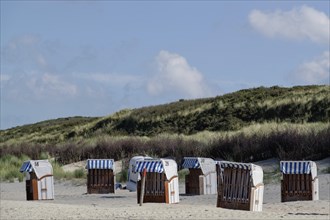 Several beach chairs on the beach with grassy dunes and blue sky in the background, Spiekeroog,