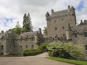 Historic castle with towers and green vegetation under a cloudy sky, old grey stone building in a