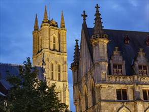Gothic church tower and building facades, illuminated at dusk, blue hour in a medieval town with