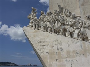 Large stone monument with several figures along the coast under a blue sky, Lisbon, Portugal,