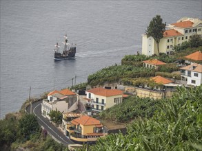 Coastal town with houses on a hill and a ship on the blue water, Madeira, Portugal, Europe