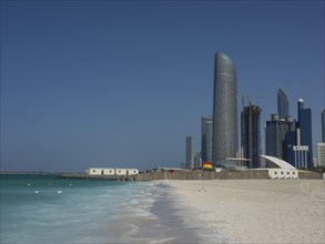 Coastal scene with a modern skyscraper and neighbouring buildings on a sandy beach under a clear