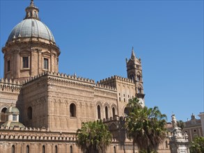 Historic cathedral with towers and a dome, surrounded by palm trees under a clear blue sky, palermo
