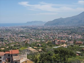 A wide panorama over a city with houses, green hills and the sea in the background, palermo in