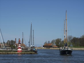 A large boat navigates through the harbour with a lighthouse and buildings in the background,