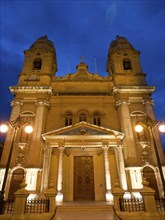Illuminated church facade at night, with two towers, lamps and decorative elements, Valetta, Malta,