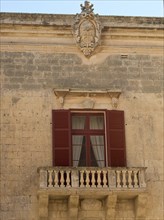 Historic facade with red shutters and small stone balcony, the town of mdina on the island of malta