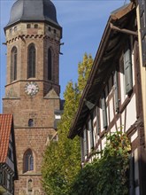 Stone church tower and half-timbered houses with autumn leaves under a blue sky, historic