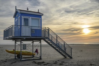 A blue and white rescue tower with a secured boat next to it, in front of an idyllic sunset on the