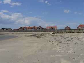 Empty beach with traces in the sand and traditional buildings in the background, Baltrum Germany